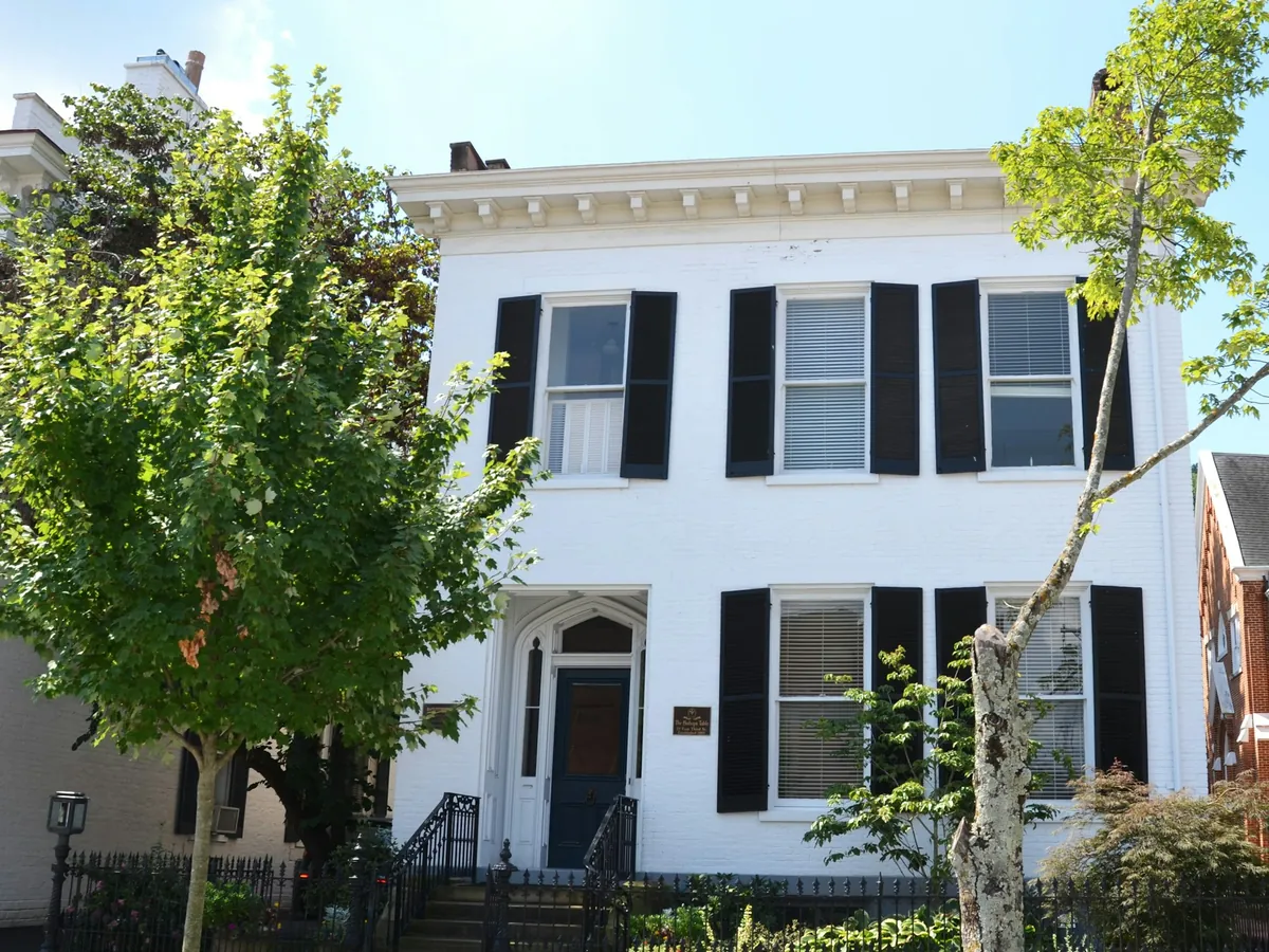 A white two-story house with black shutters on a tree-lined street