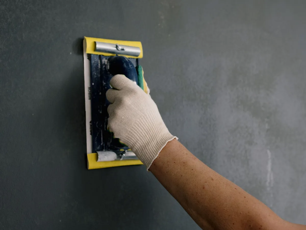 A gloved hand sanding a wall with a sanding block