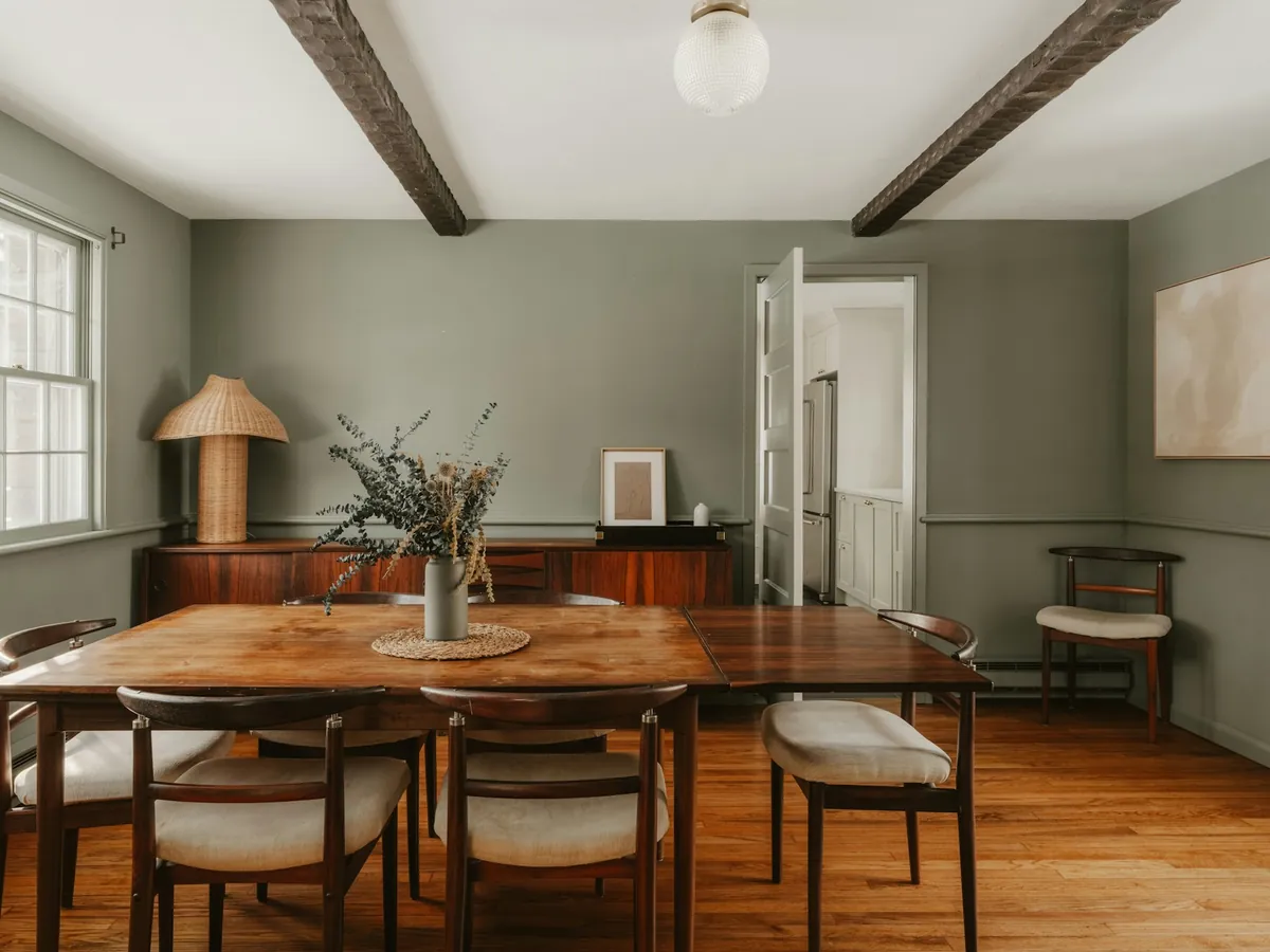 A dining room with sage green walls, white trim, and wood beams