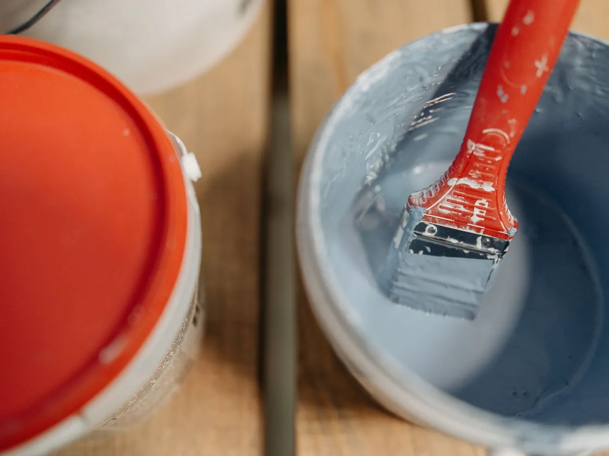 A paintbrush resting in a bucket of blue-grey paint